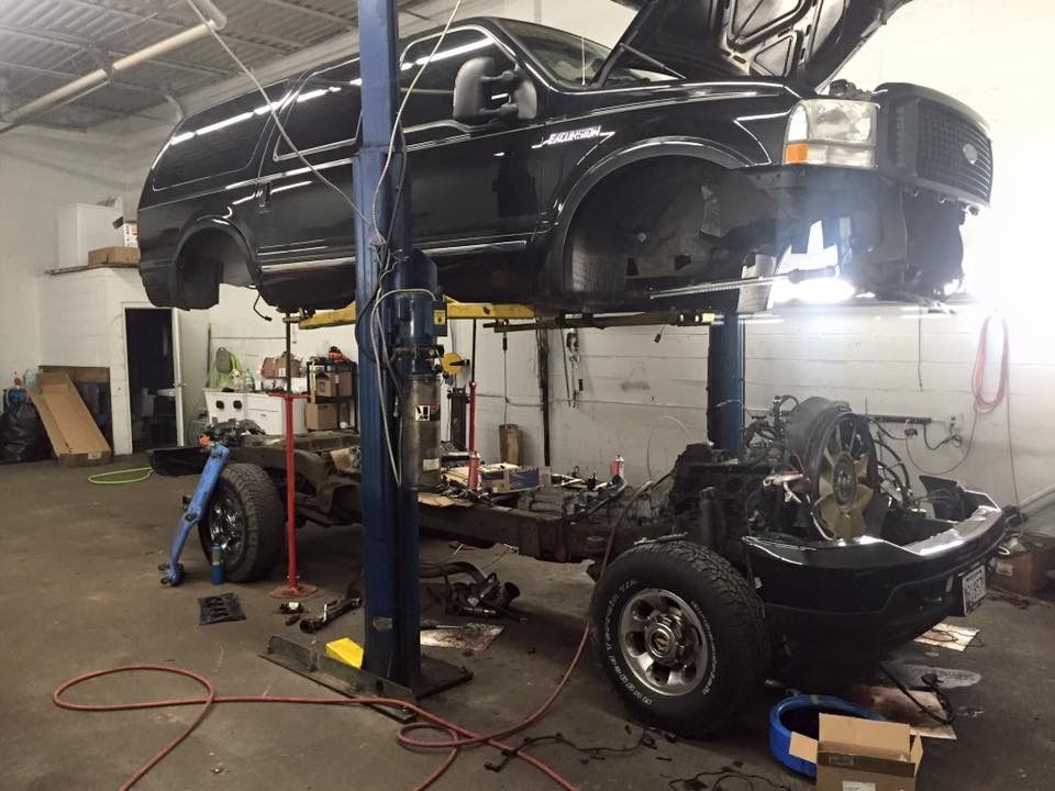 Black Ford Excursion on a car lift with the body separated from the frame in a garage.