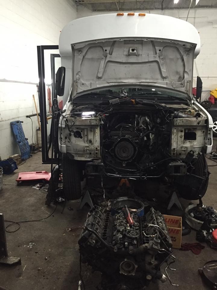 A white bus with its hood open, revealing the engine, which sits on the floor; in a garage.