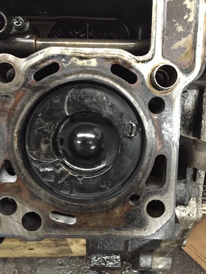 Engine cylinder head with a piston visible. The piston is black, and the surrounding metal is silver.