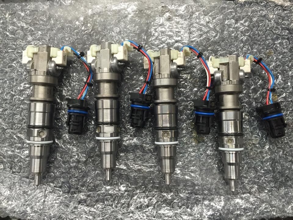 Four diesel fuel injectors with wiring harnesses, lying on crinkled silver material.