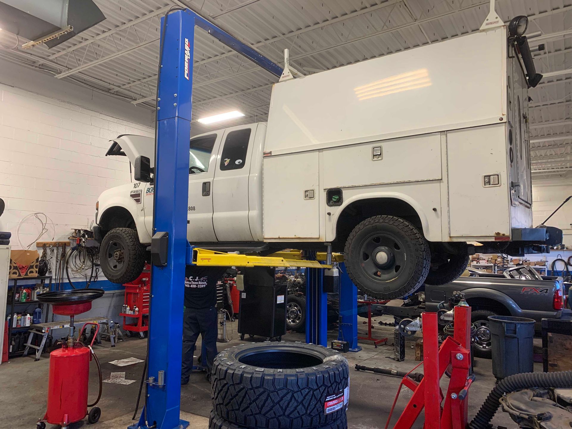 White truck raised on a blue lift in a garage, a person stands nearby with tires.