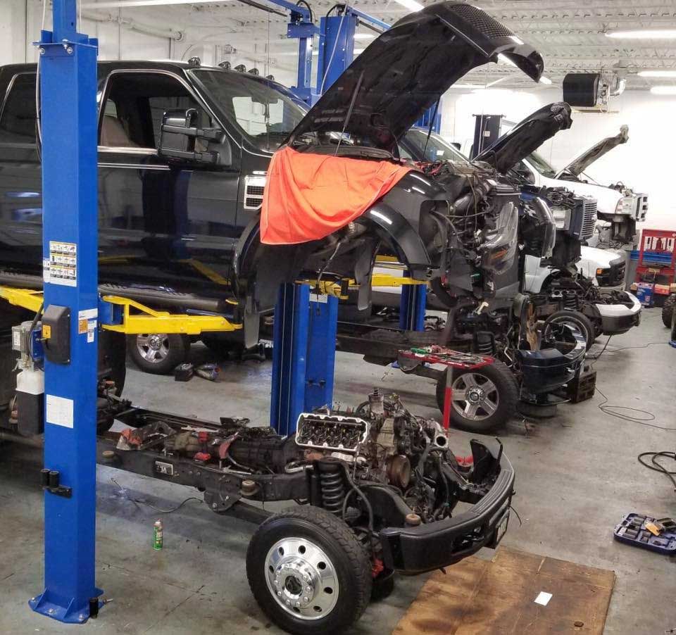Trucks on lifts in an auto repair shop; hoods open, engines exposed for maintenance.