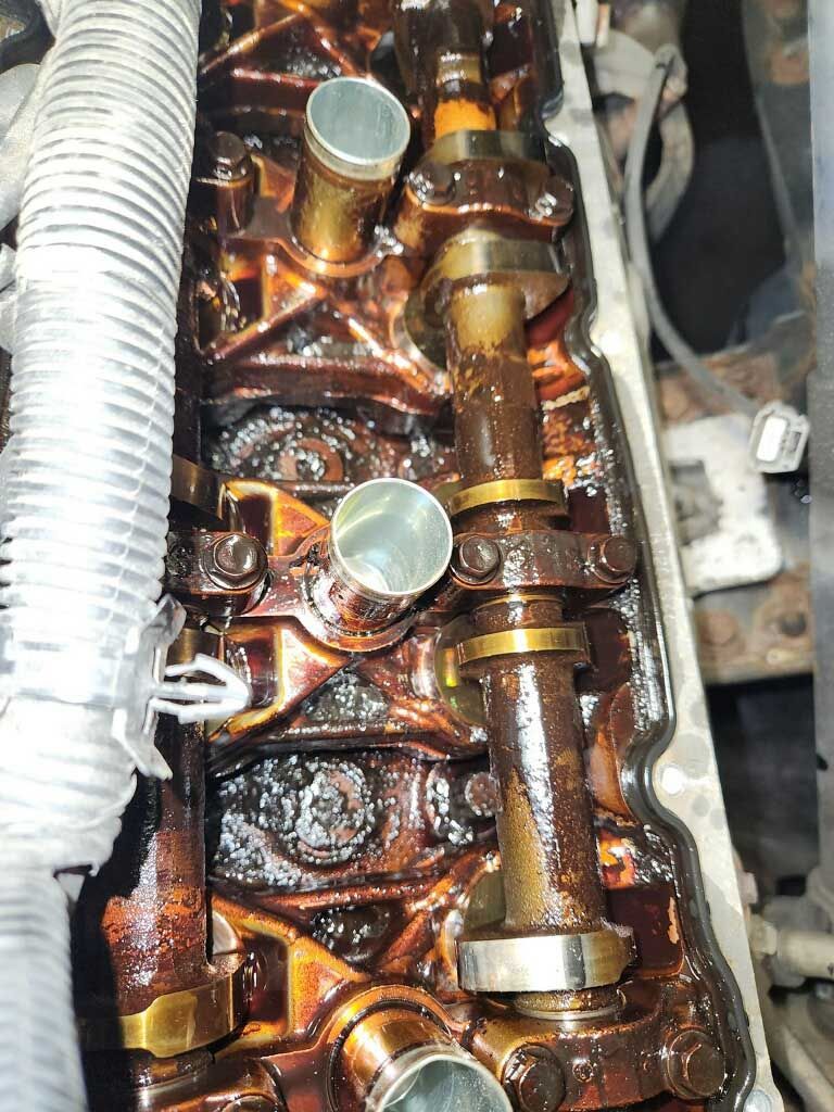 Engine parts coated in brown oil, camshafts and valve stems visible.