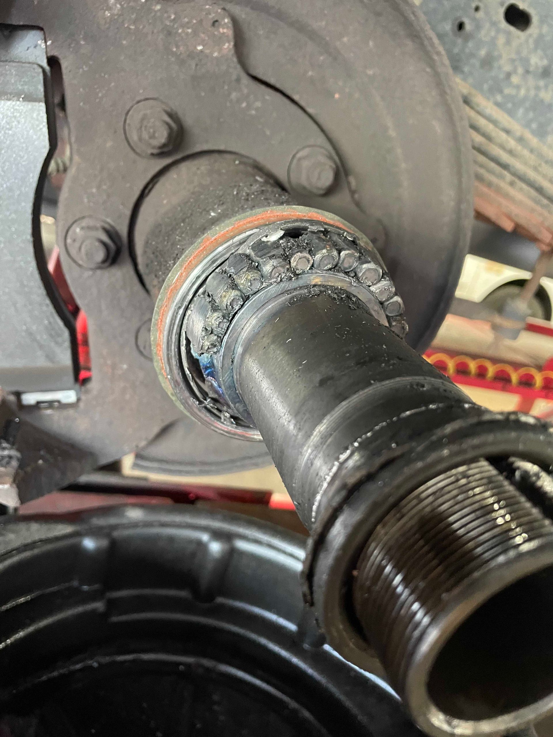 Close-up of a damaged vehicle axle with exposed bearings, a black oil pan in the foreground.