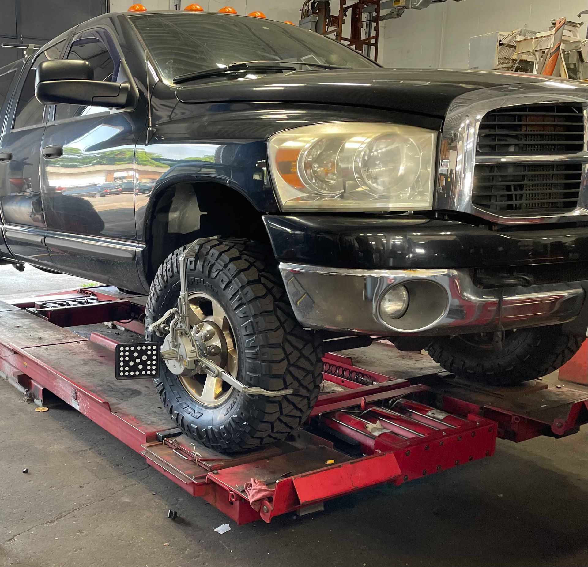 Black pickup truck on a red alignment rack, undergoing wheel alignment in a garage.
