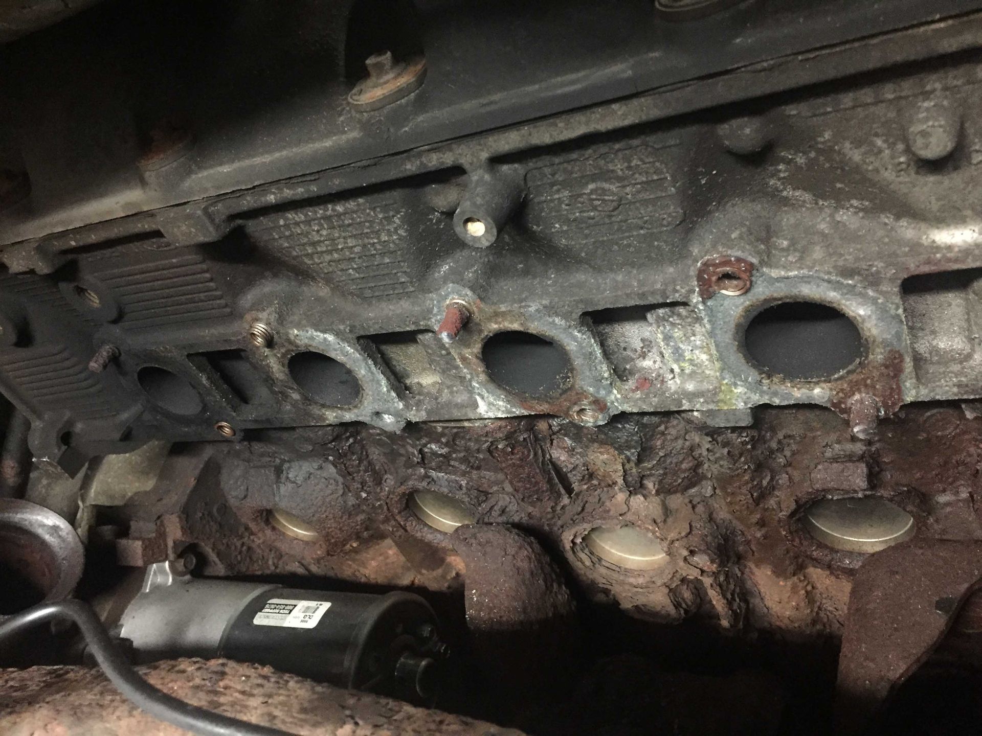 Close-up view of an engine, revealing the exhaust manifold and cylinder head ports. Visible rust and oil stains.