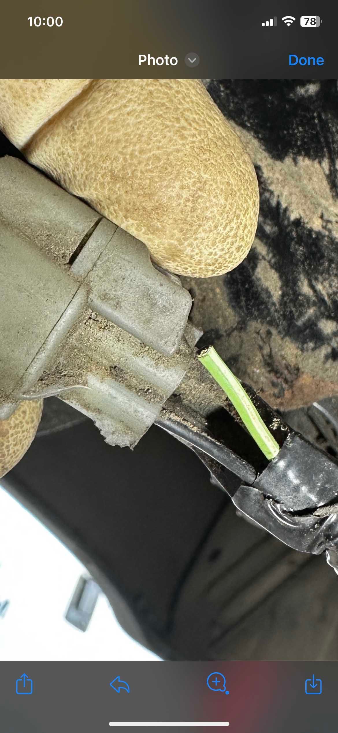 A cut green wire being held by pliers, near a vehicle part.