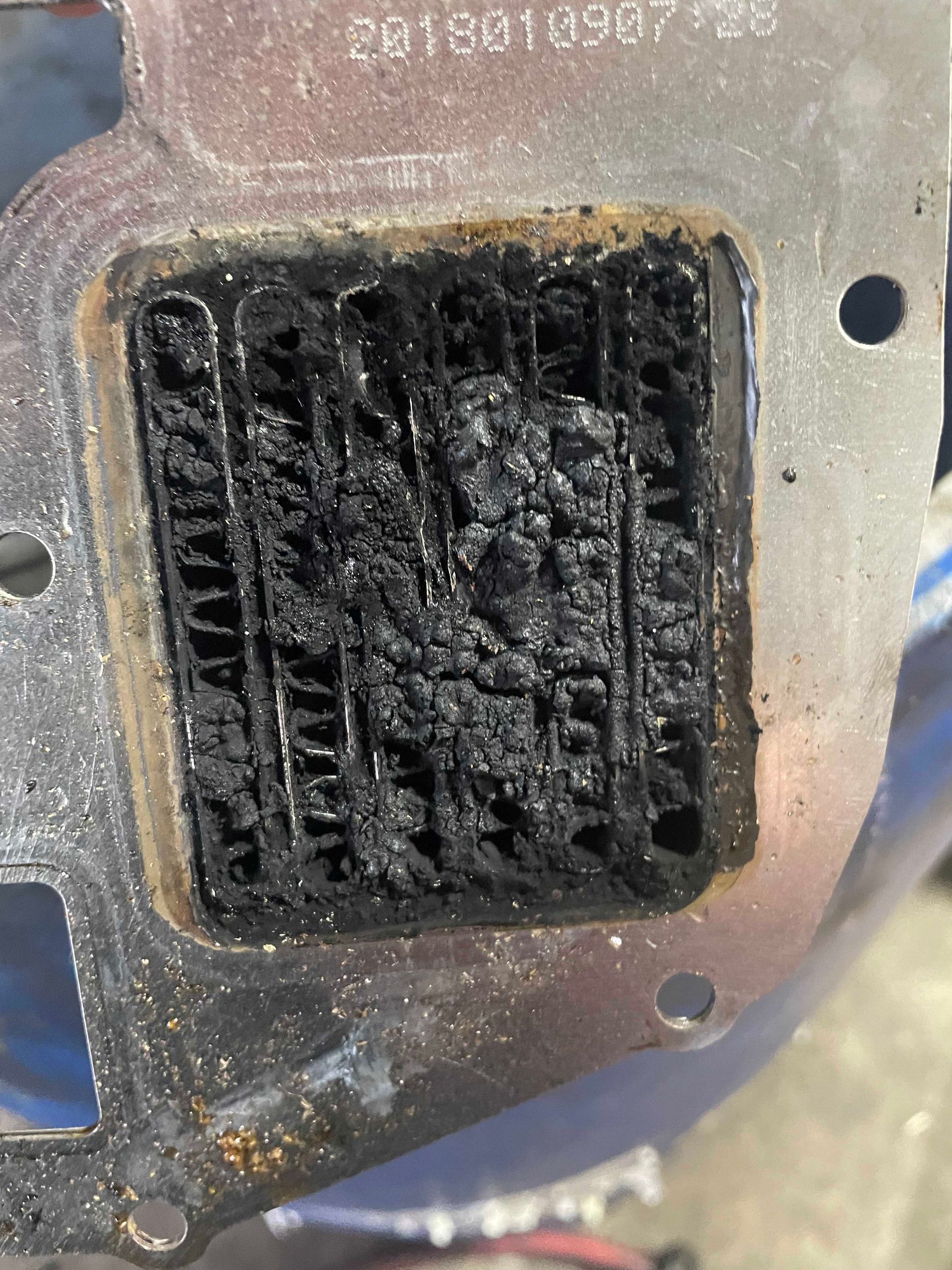 A metal EGR cooler with heavy carbon buildup, rectangular with a grid pattern.