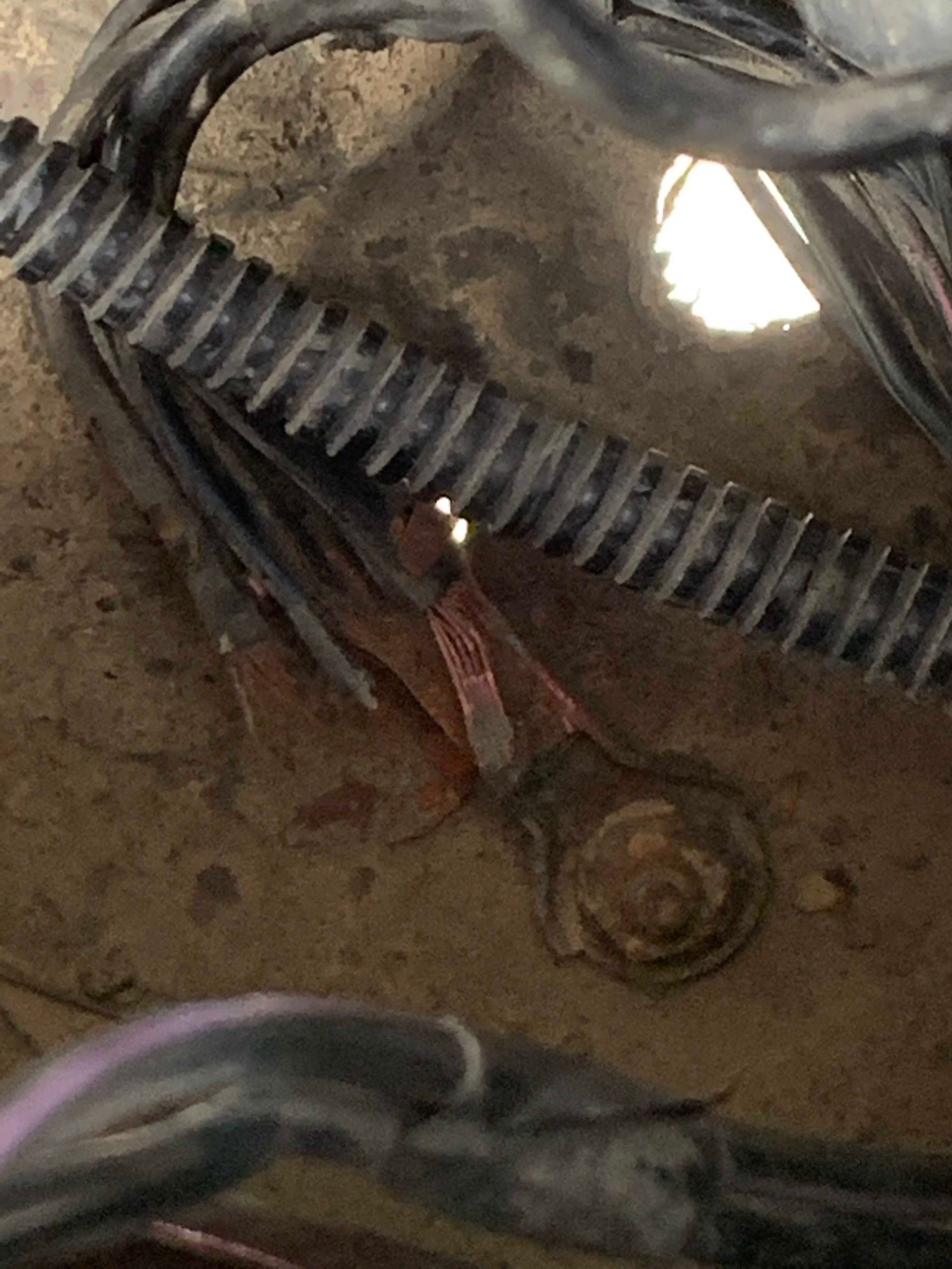 Close-up of car wiring; black wires with protective tubing, a rusty ground terminal.