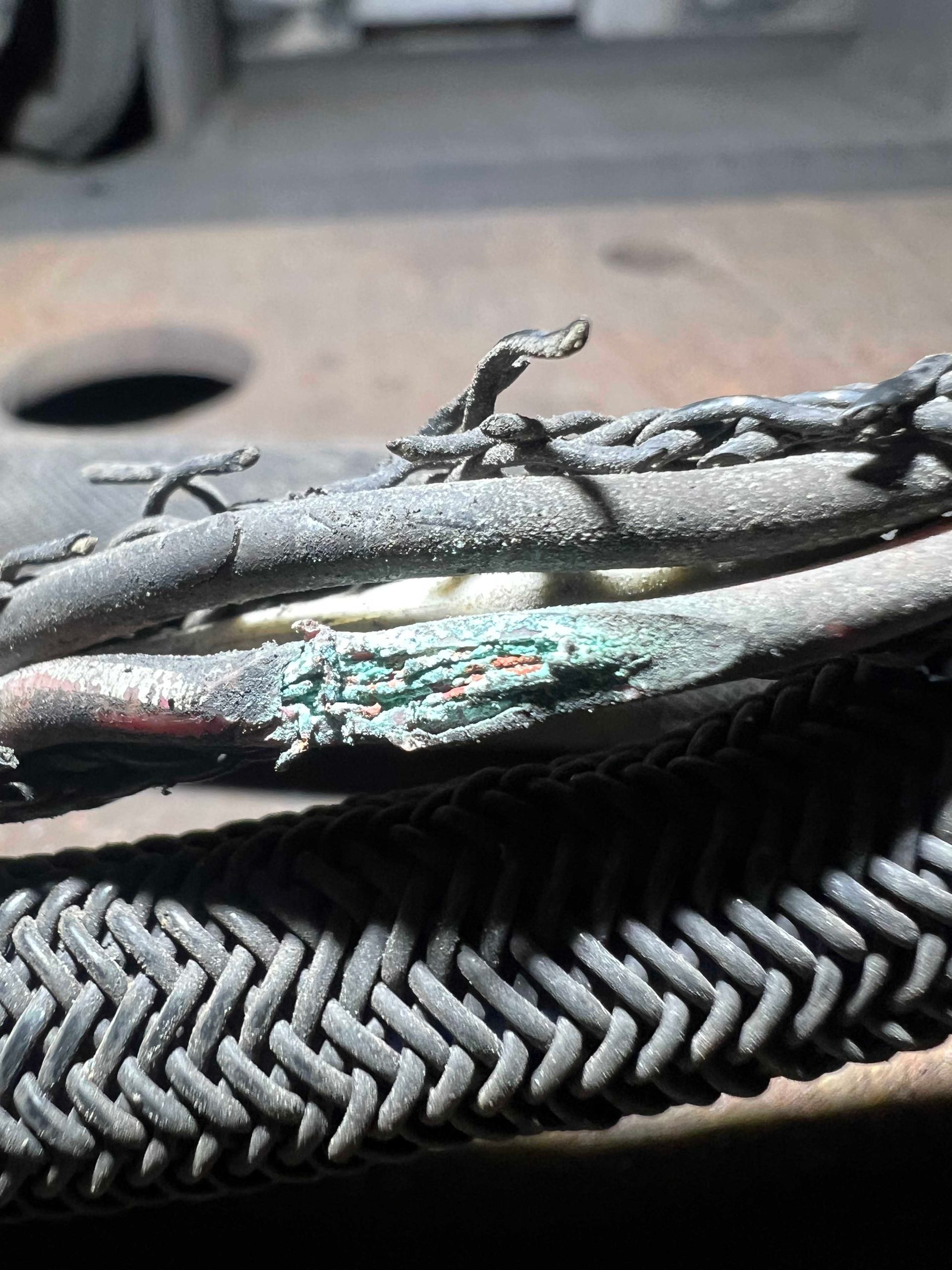 Damaged electrical cable, showing exposed wires with corrosion. Braided sheath visible.