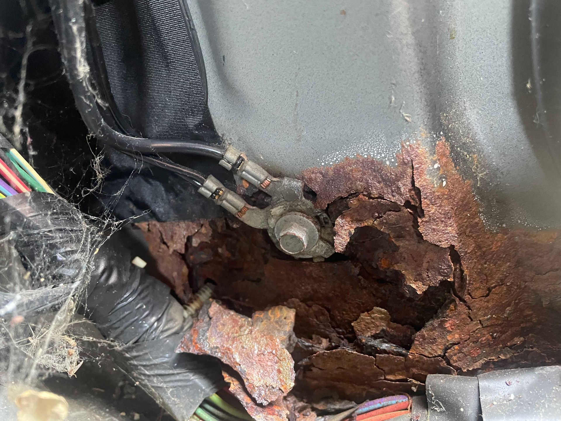 Severe rust damage around a bolted electrical ground in a vehicle's metal body.