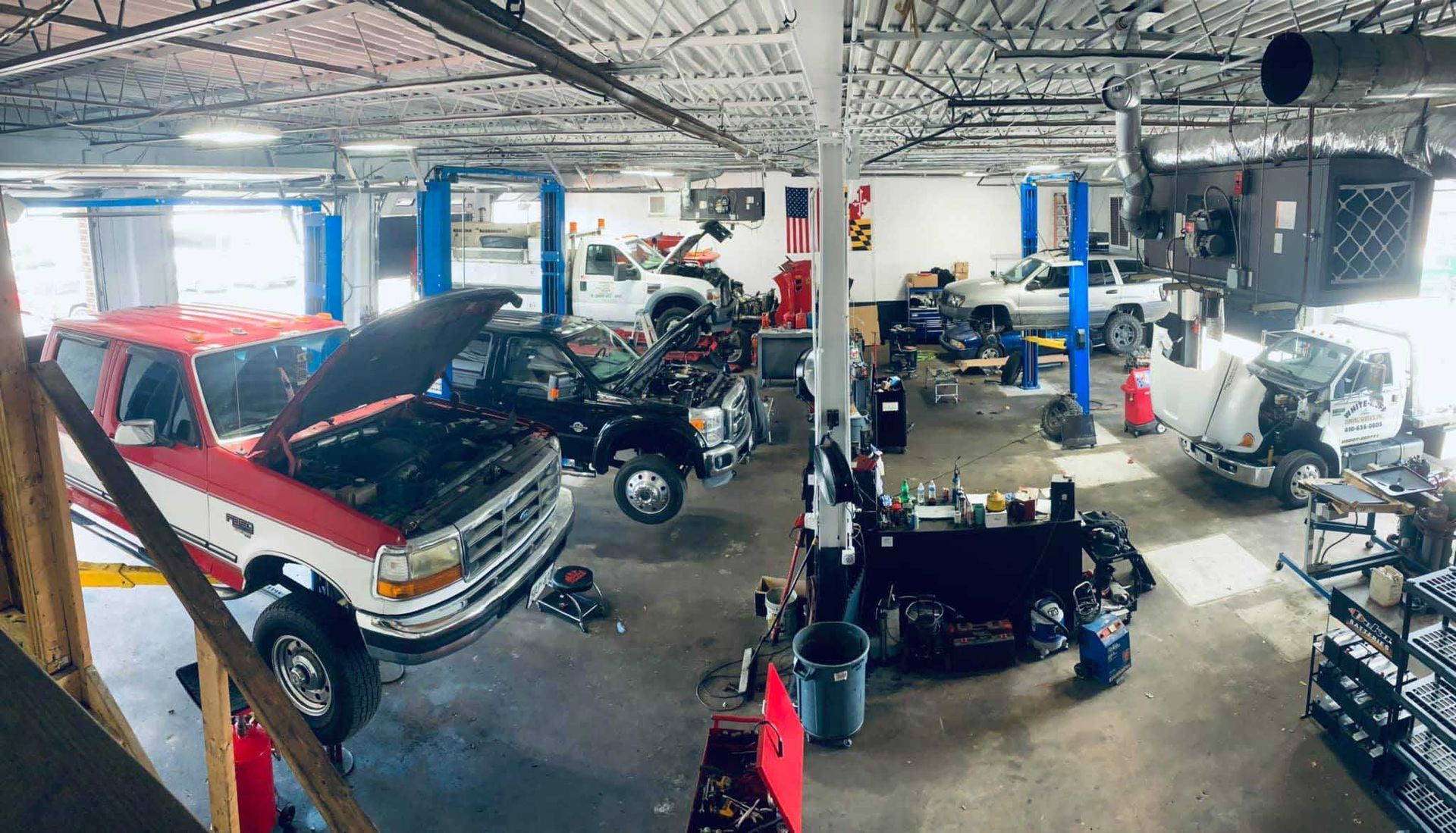 Wide shot of an auto repair shop with multiple vehicles on lifts, red and white truck in foreground.