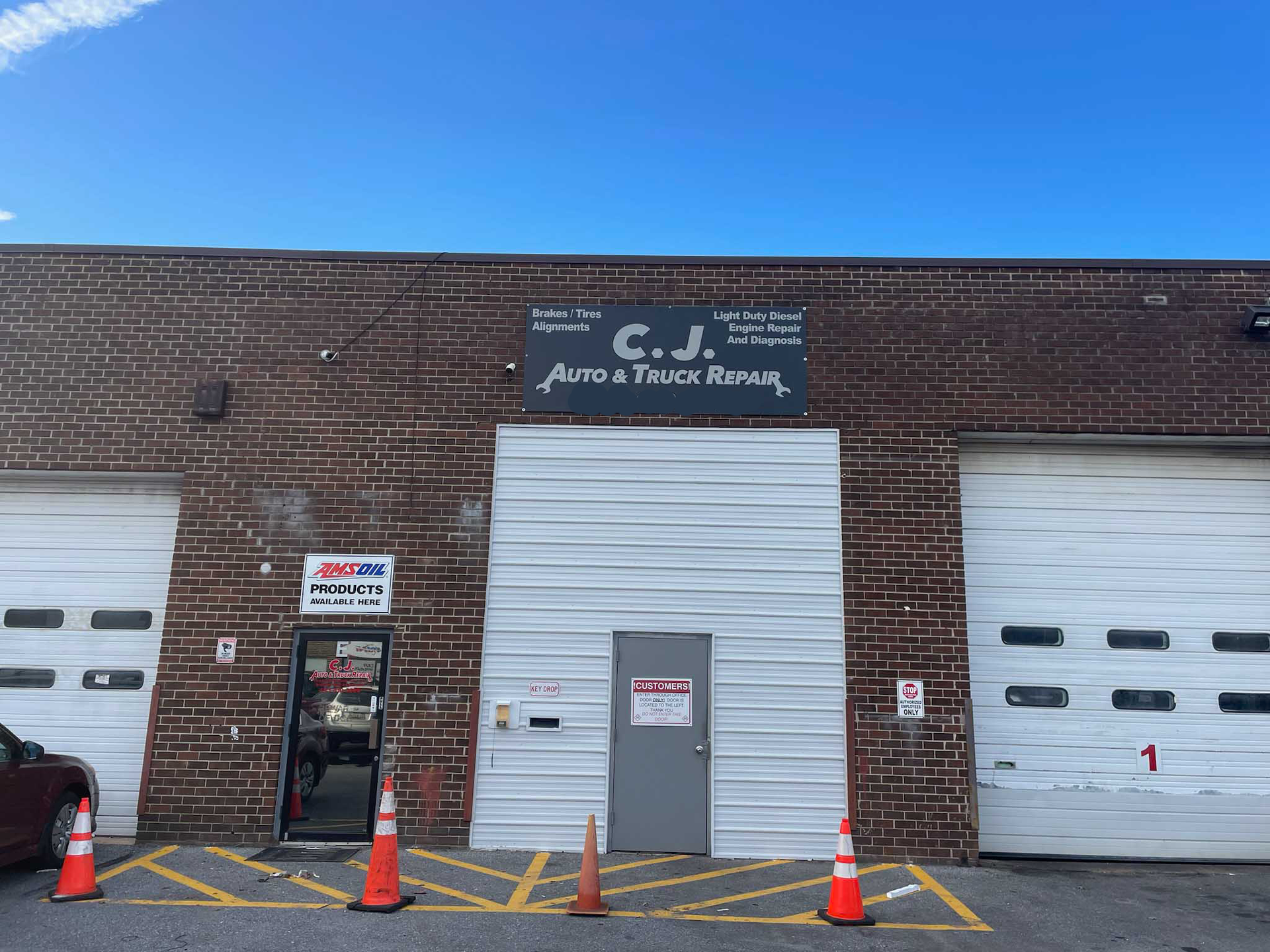 Exterior of a brick building with garage doors; sign reads “C.J. Auto Parts & Repair.” Blue sky.