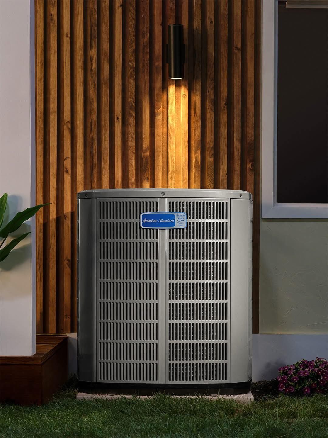 Outdoor HVAC unit against a wood slat wall with a light above it