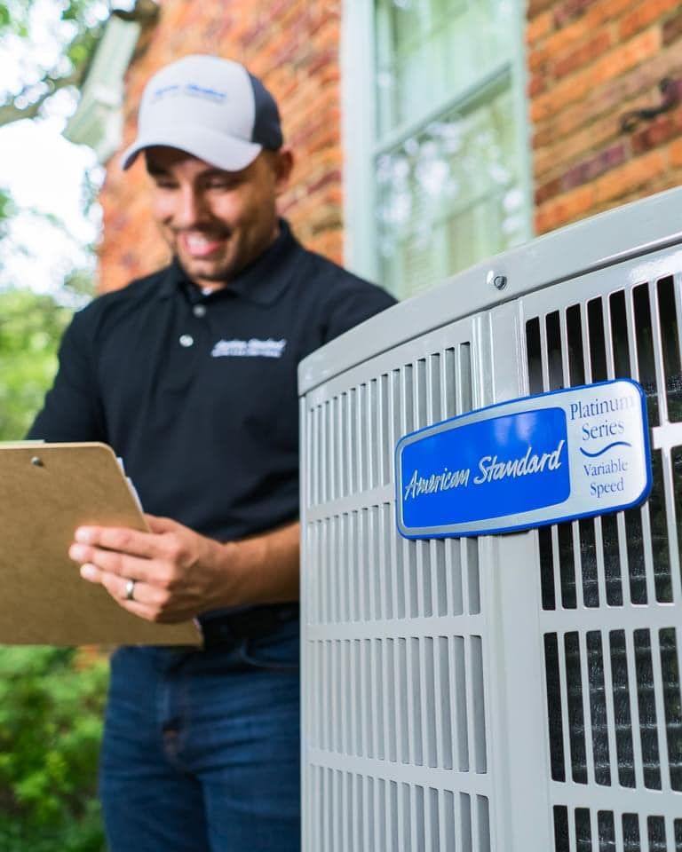 Technician smiling at a tablet beside a large outdoor HVAC unit with a blue service label