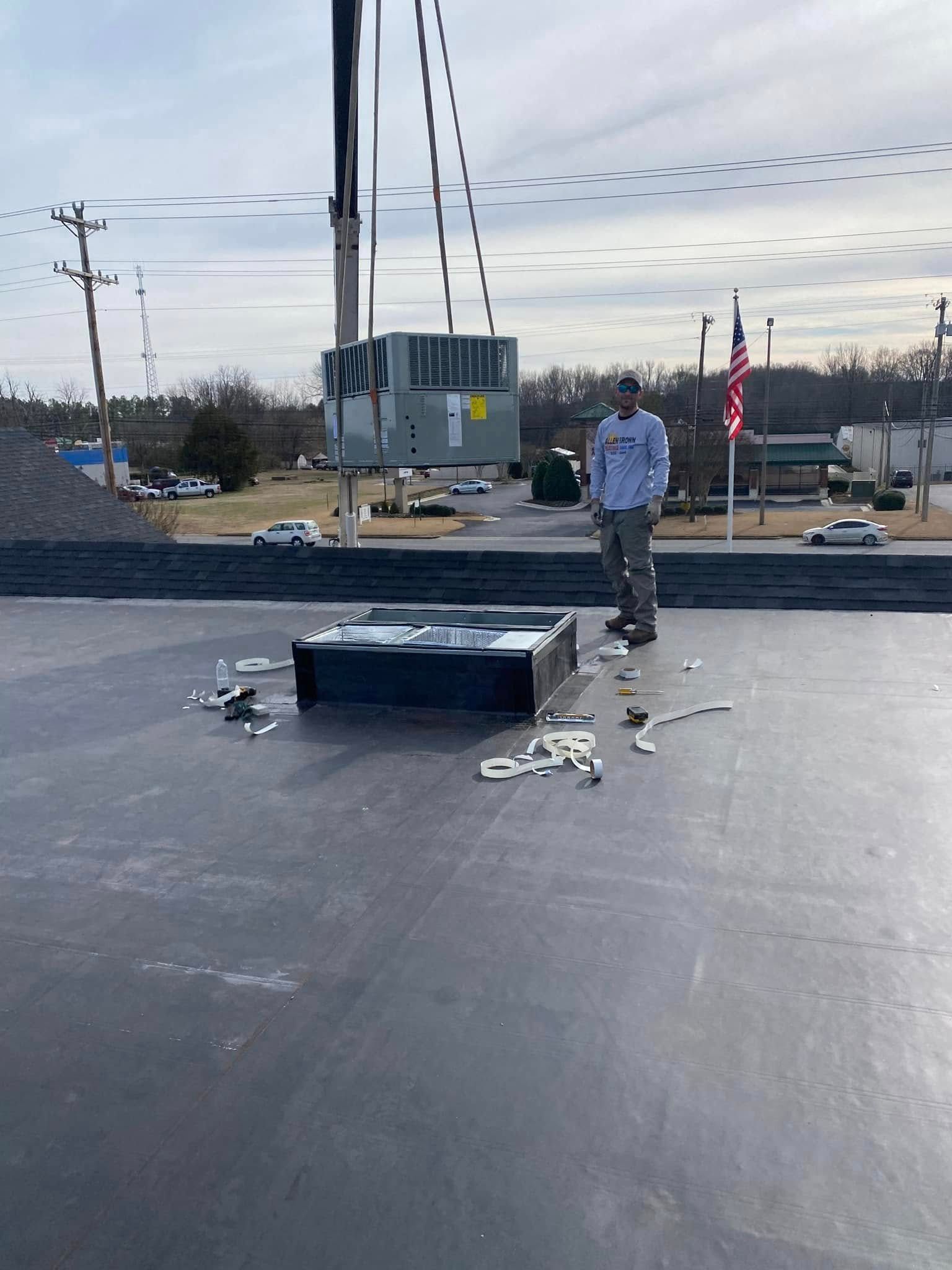Worker on a flat rooftop near a vent, with scattered tools and an overcast sky in the background