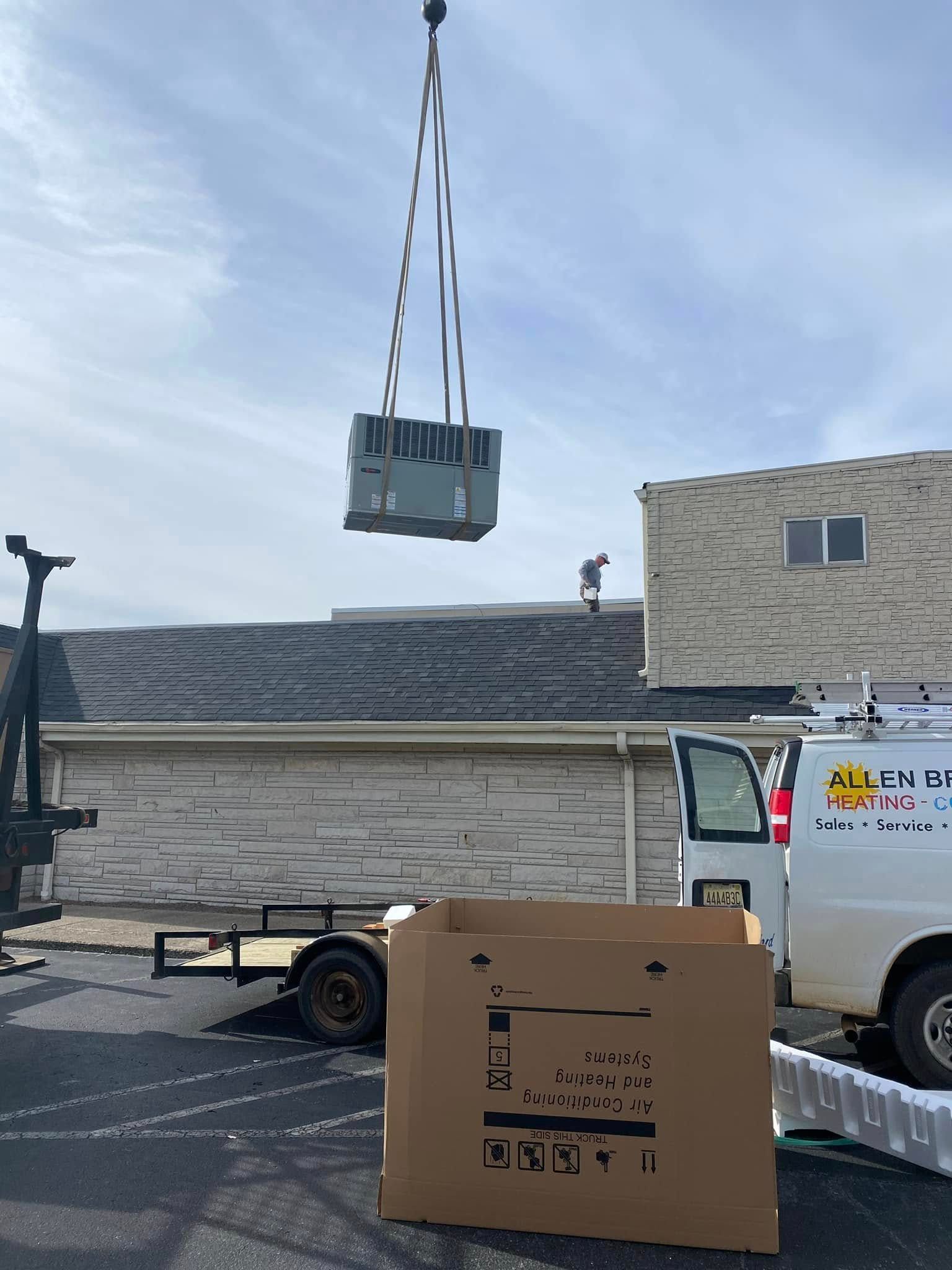 Crane lifting a crate over a flatbed truck beside a building and a white service van.