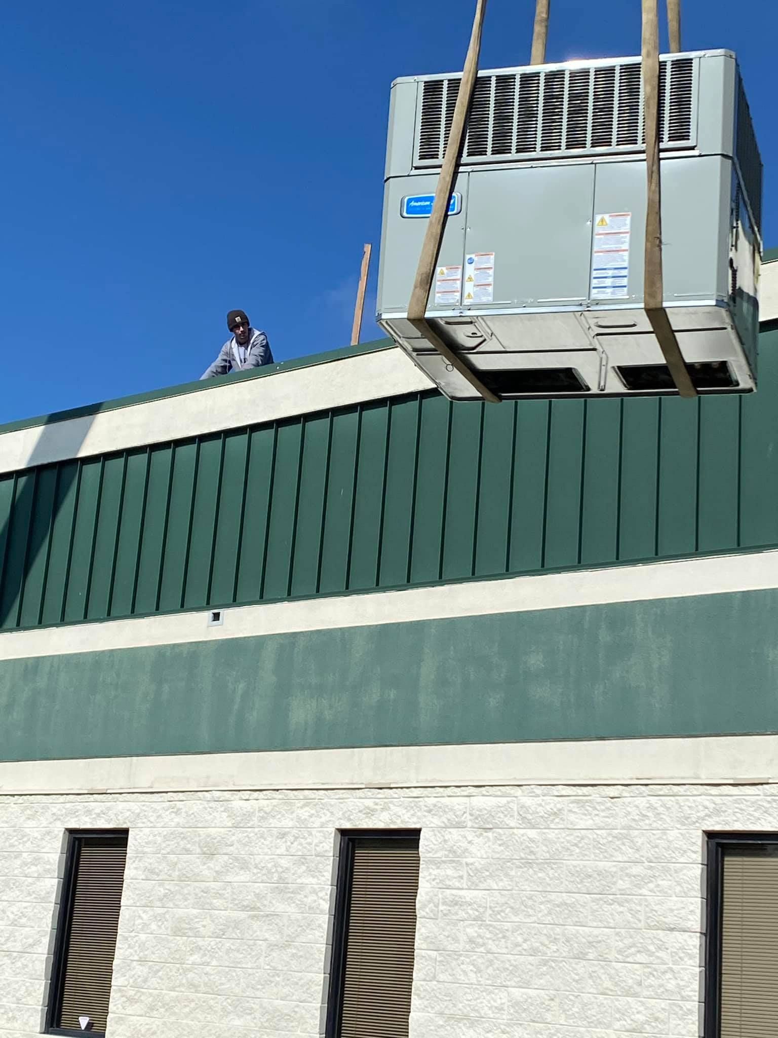 Rooftop HVAC unit on a green building, with a worker standing beside it under a clear blue sky.