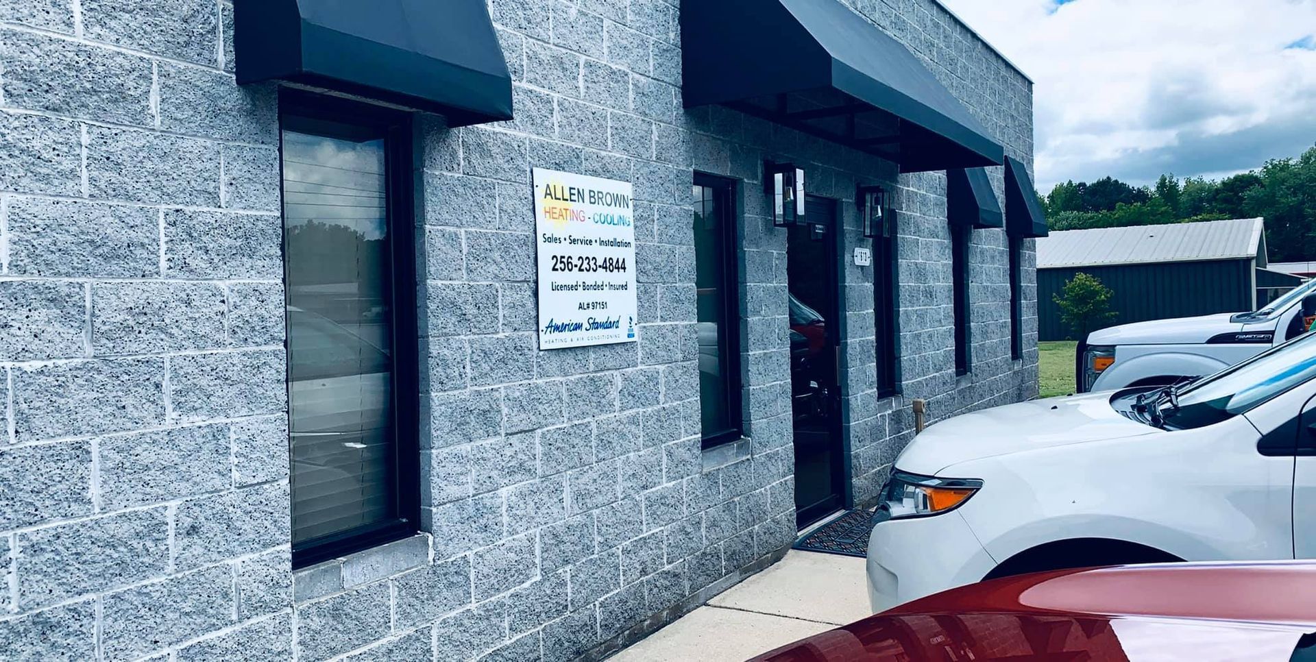 Gray building exterior with windows and a sign, beside parked cars in a lot