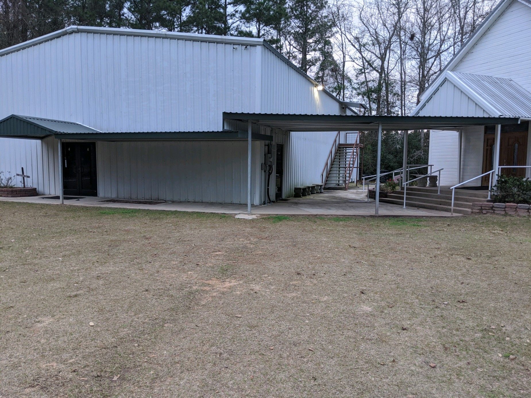 Weathered metal barn and open-sided shed on a grassy lot with trees in the background