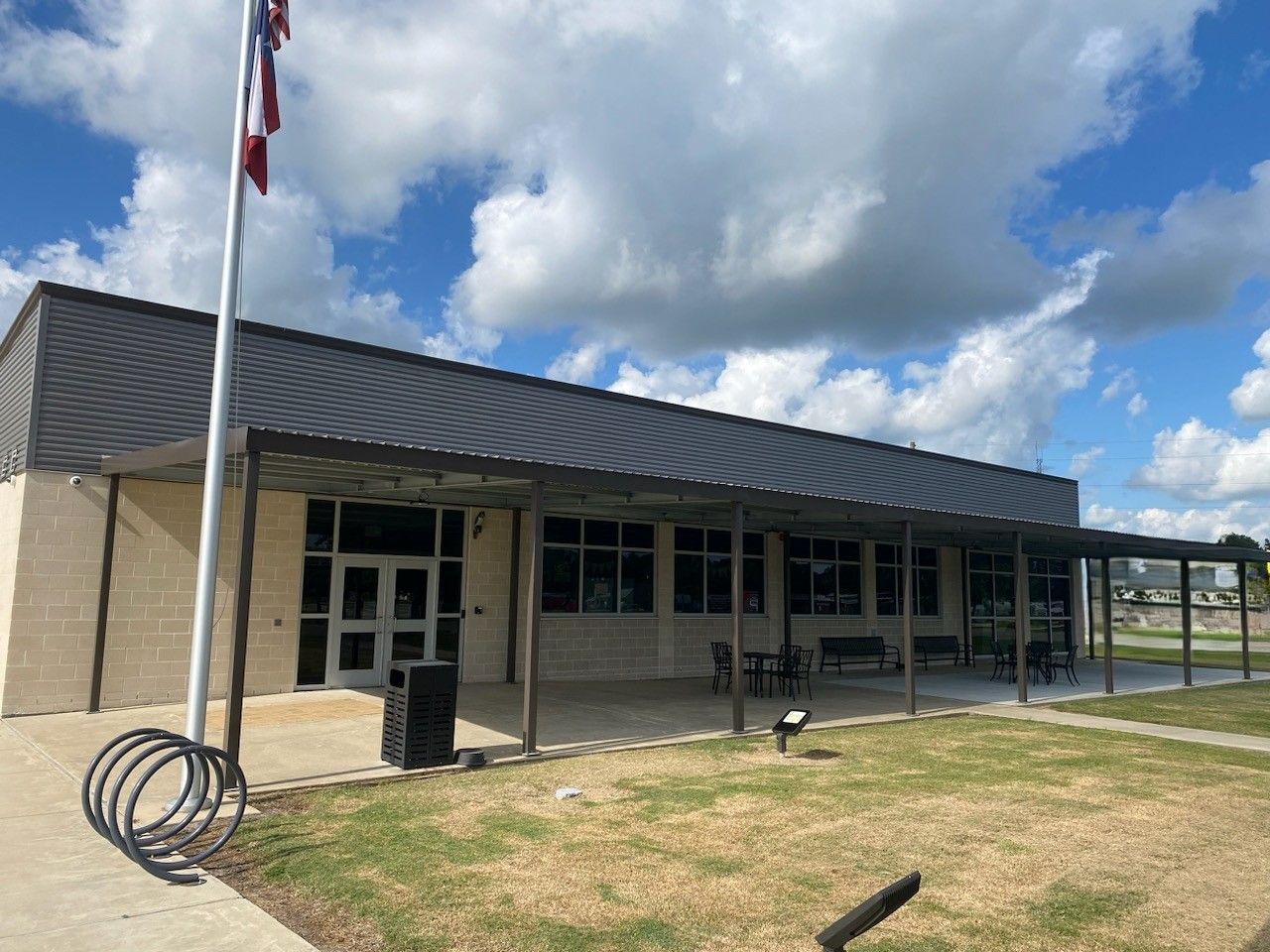 Single-story building with flagpole, covered walkway, and cloudy sky above a grassy area