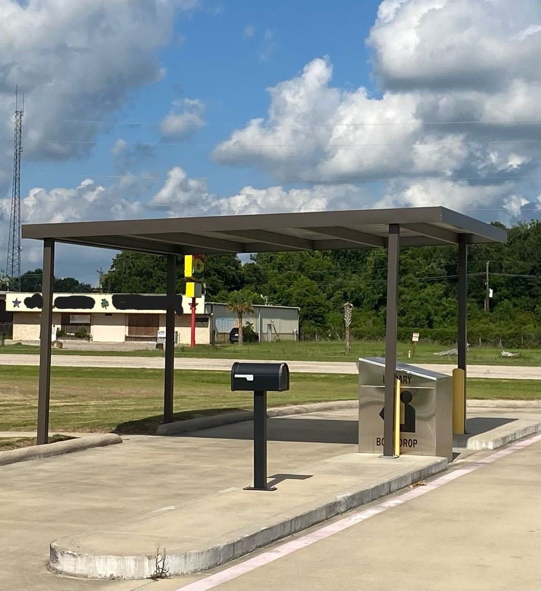 Covered outdoor grill area with a mailbox, trash bin, and concrete pad under a metal roof.