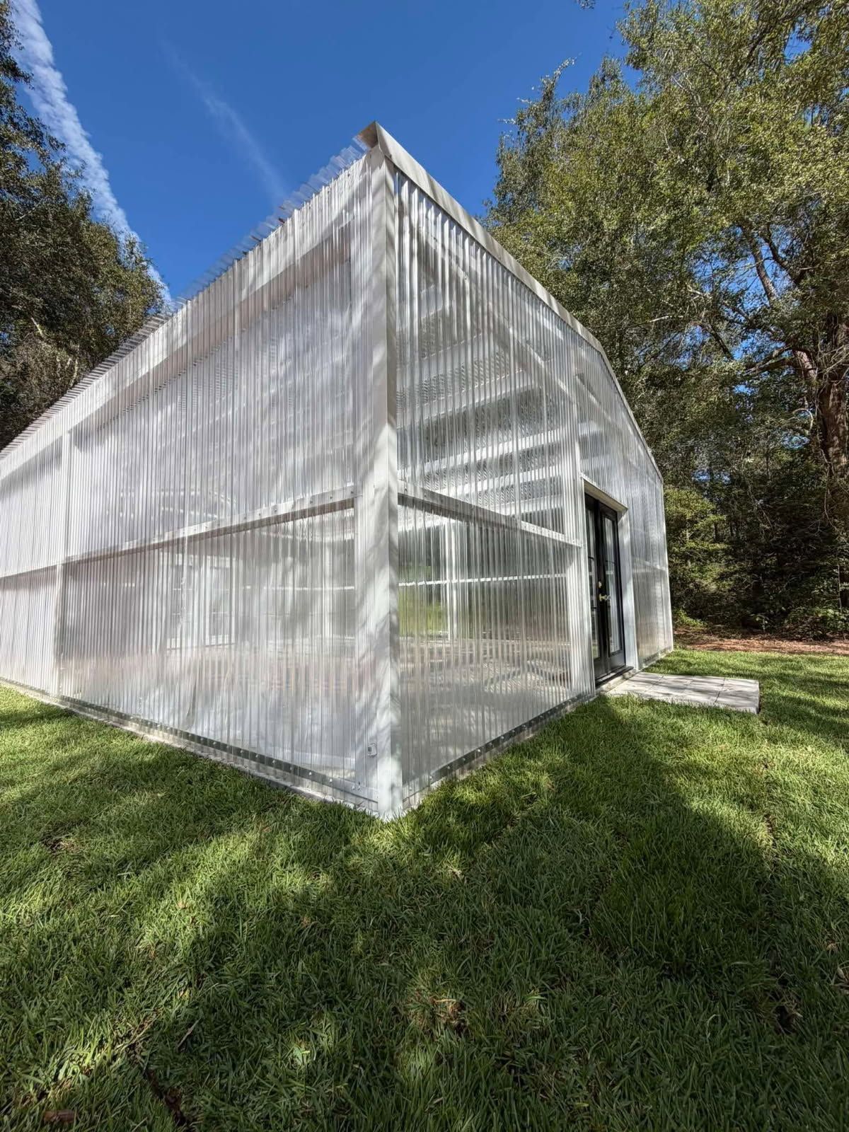 White greenhouse with translucent panels on a grassy slope under a blue sky