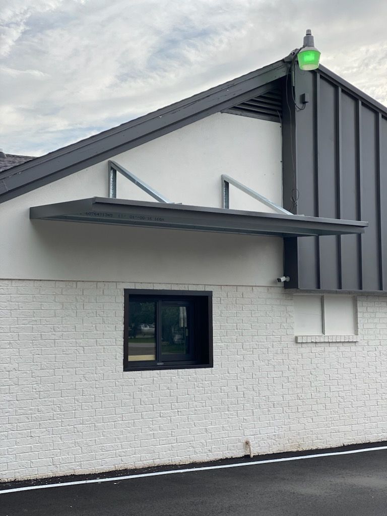 A white brick building with a black roof and a window.