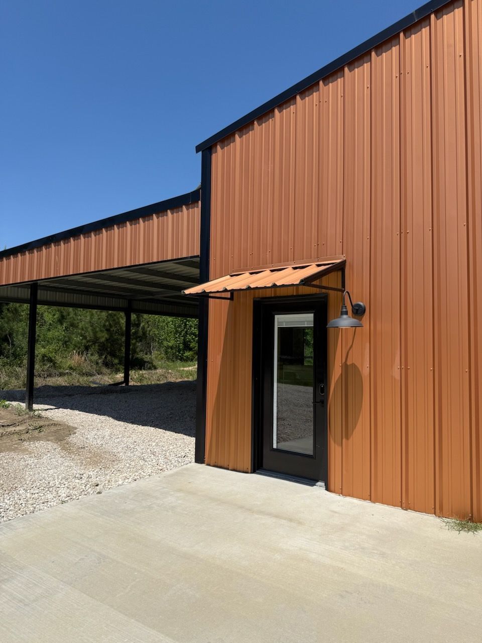 Brown metal building with black trim, carport, and concrete entrance.