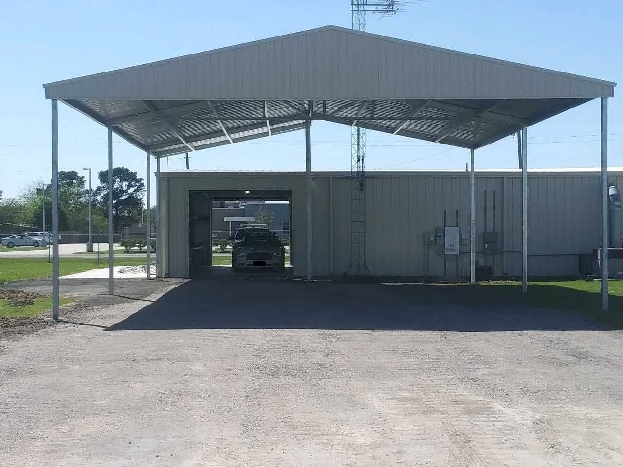 Metal carport over a gravel area, sheltering a building entrance. Bright sunlight.