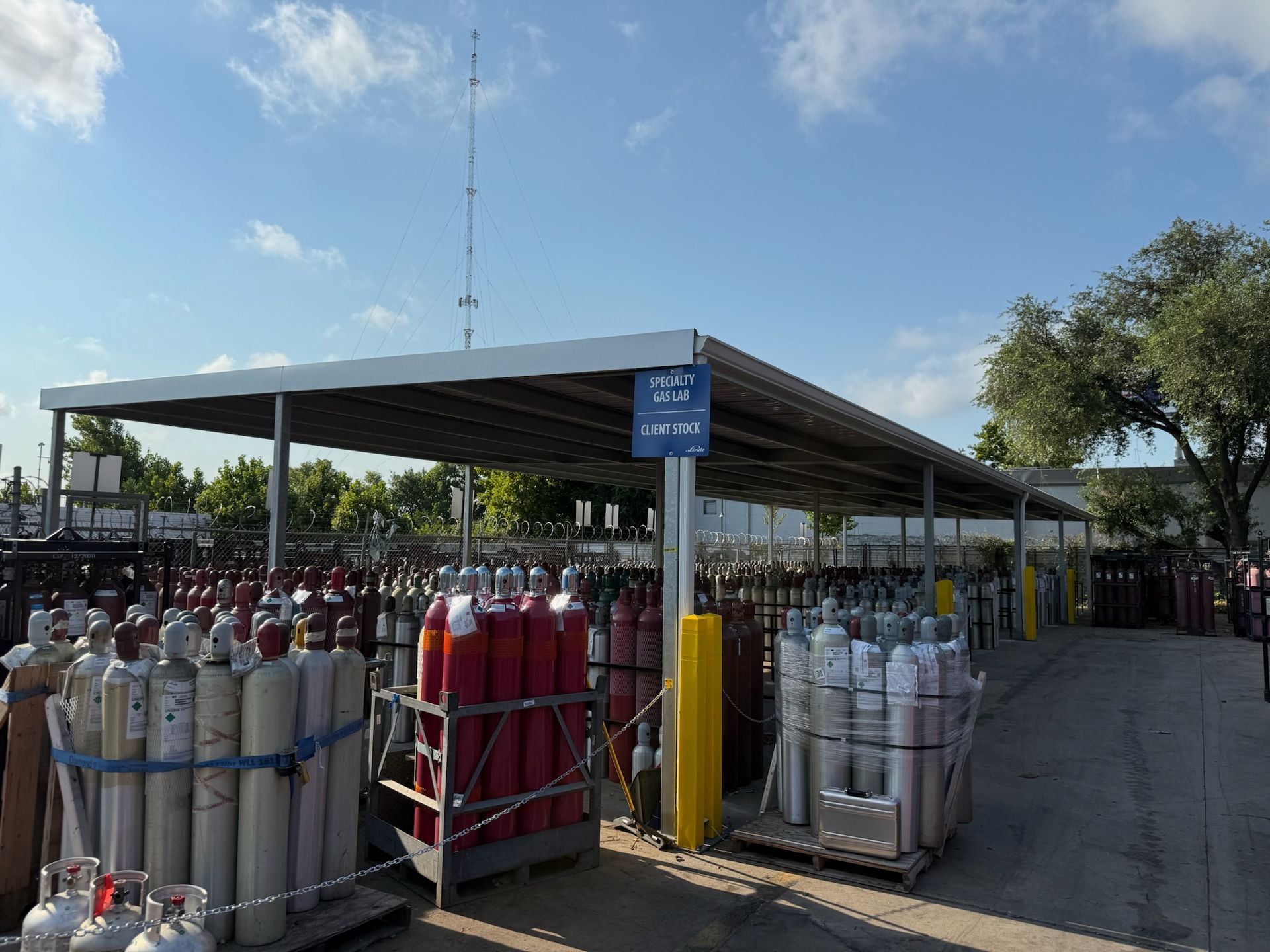Gas cylinders stored outdoors under a metal roof, blue sky above.