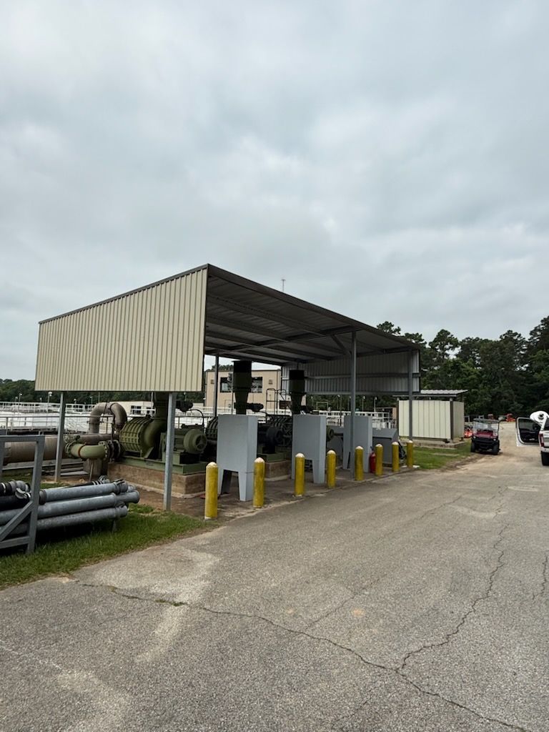 Outdoor industrial site with a metal canopy covering several gray boxes with yellow posts.