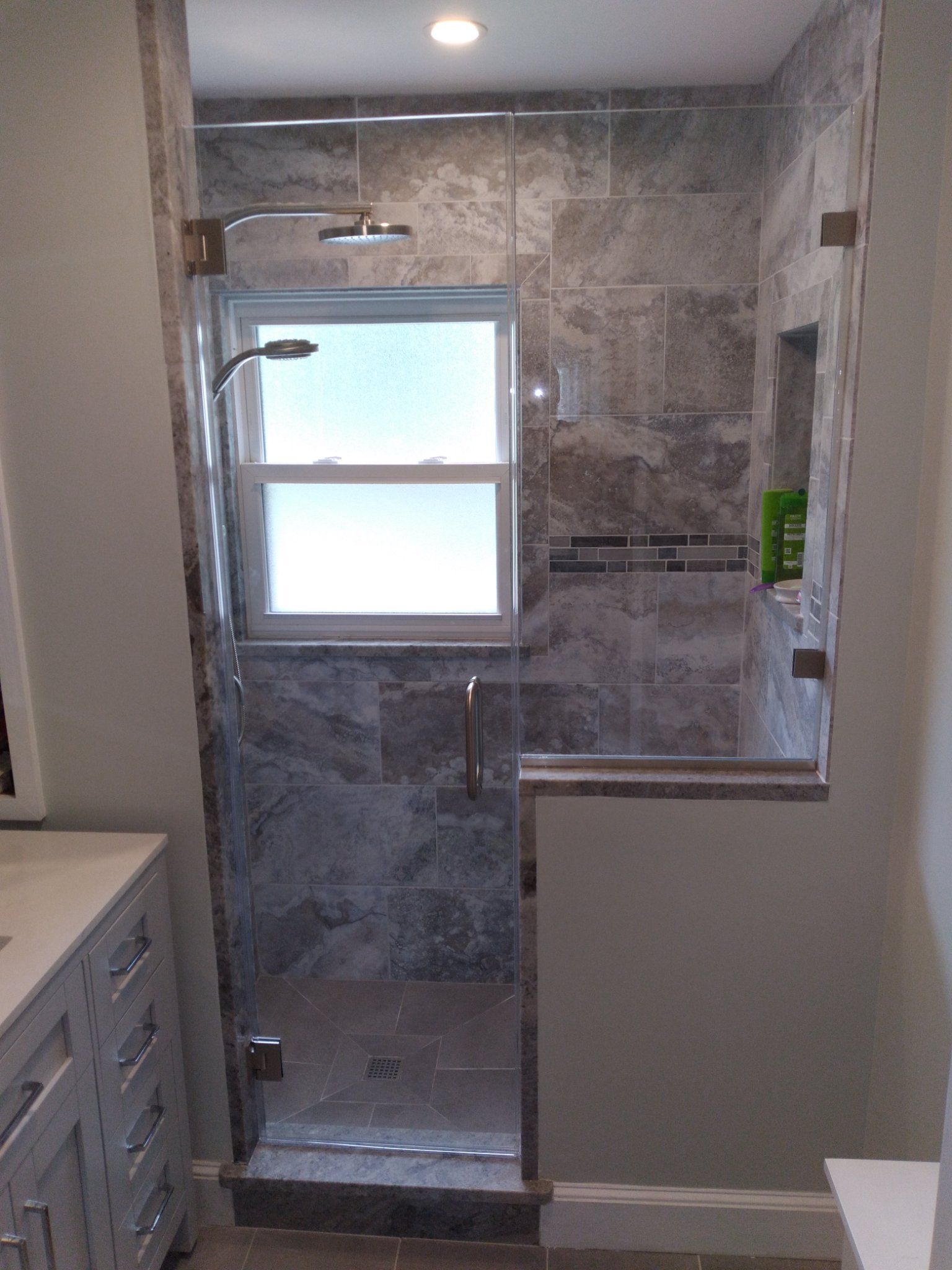 A bathroom with a glass shower door and a window.