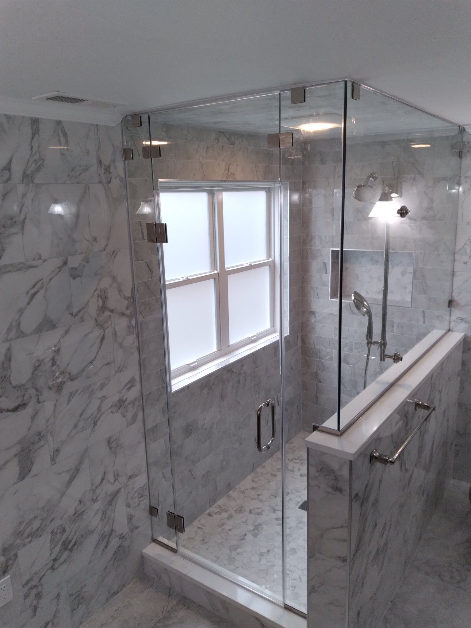 A bathroom with marble walls and a glass shower door