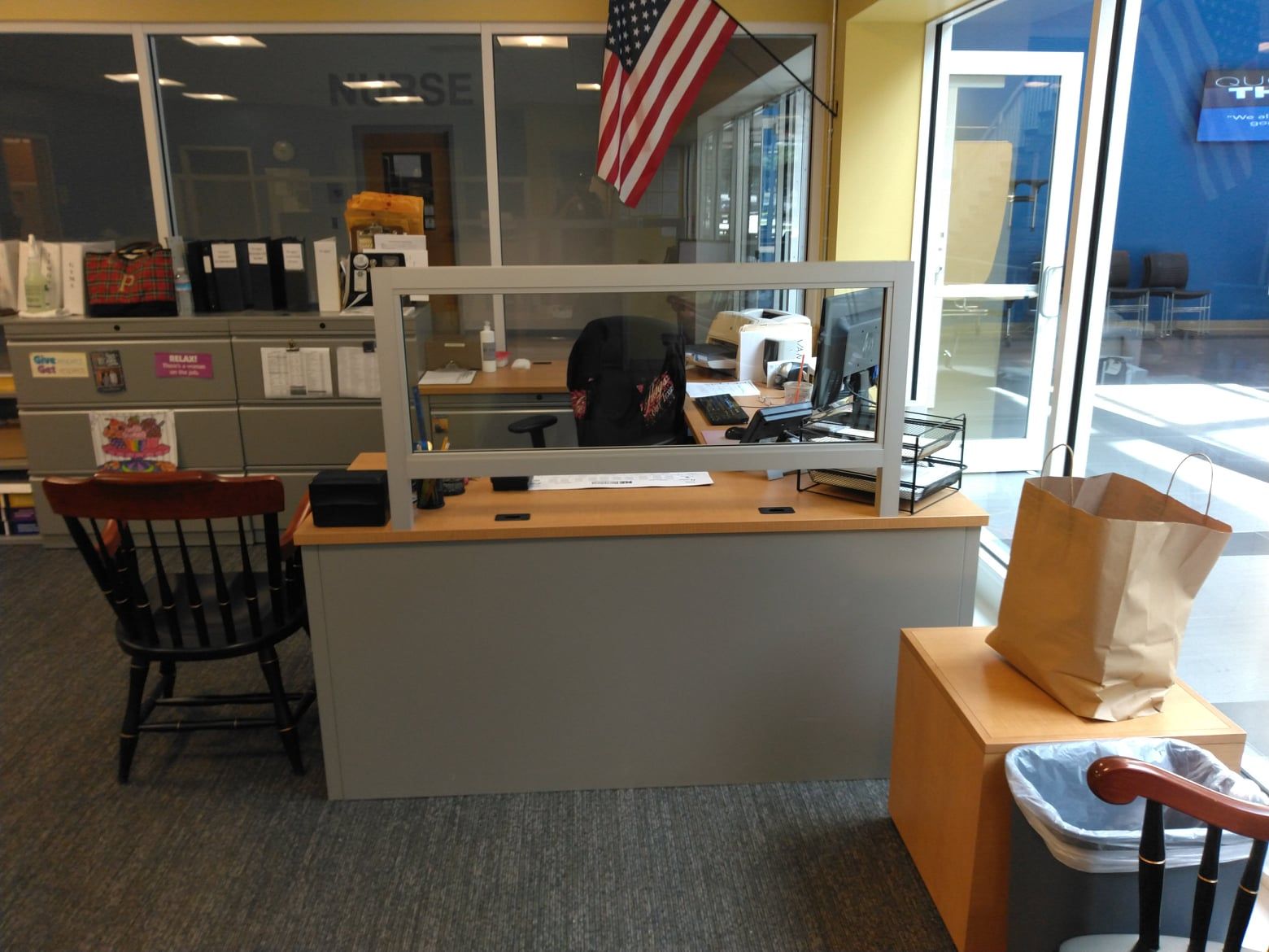 A woman sits at a desk with an american flag behind her