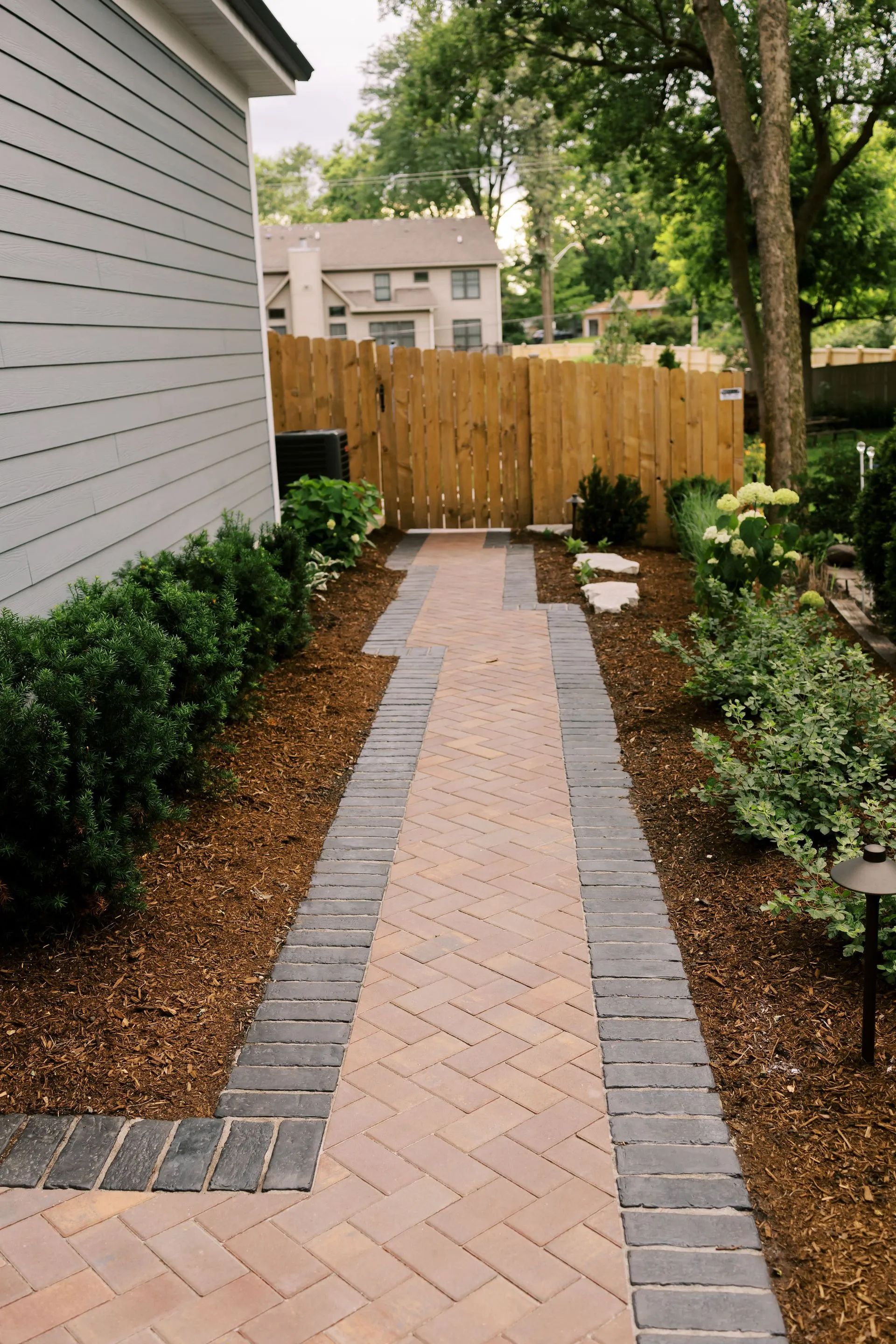 Brick pathway bordered by hedges leads to a wooden fence gate.