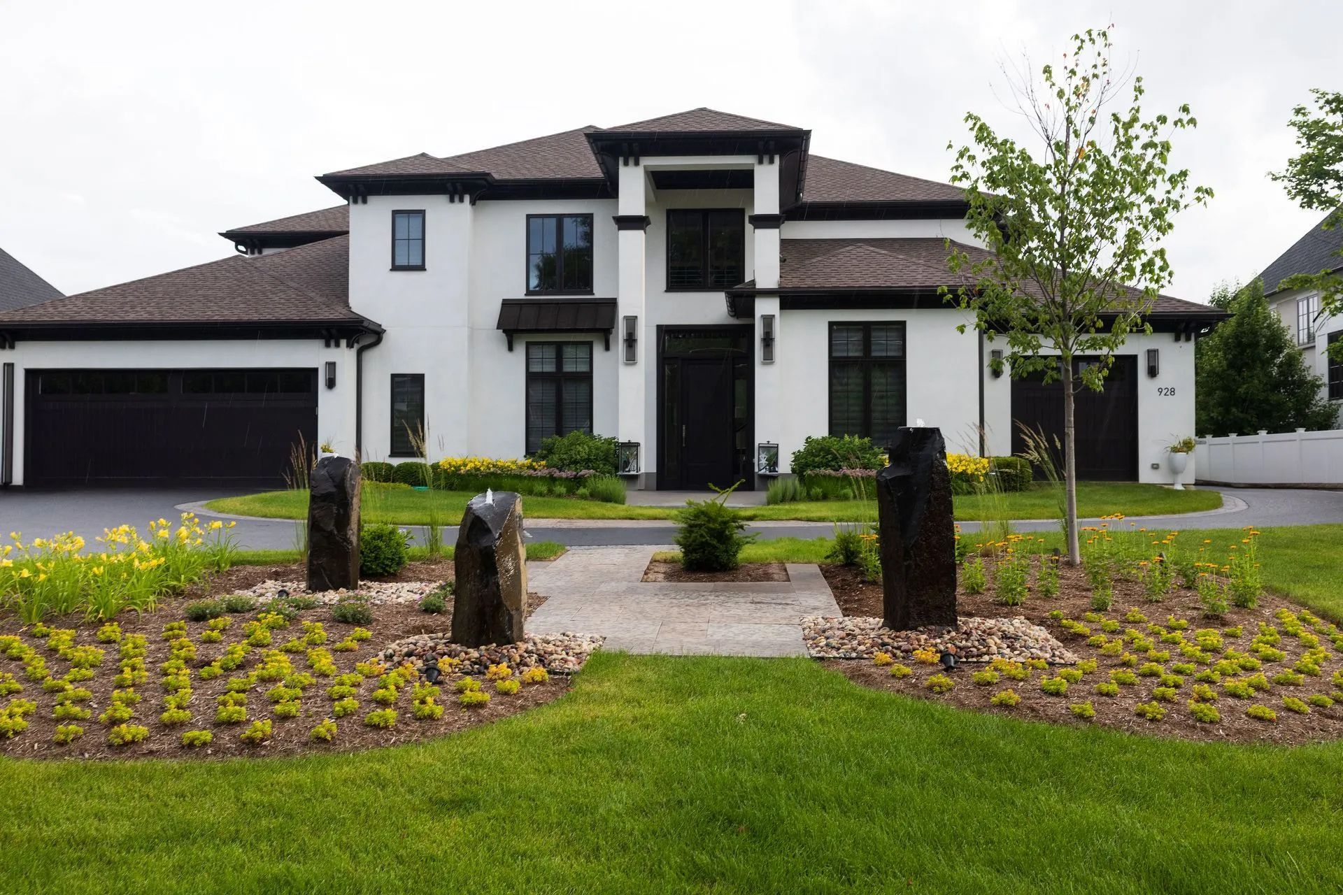 Two-story white house with black trim, black garage door, and a front yard with rock features and green grass.