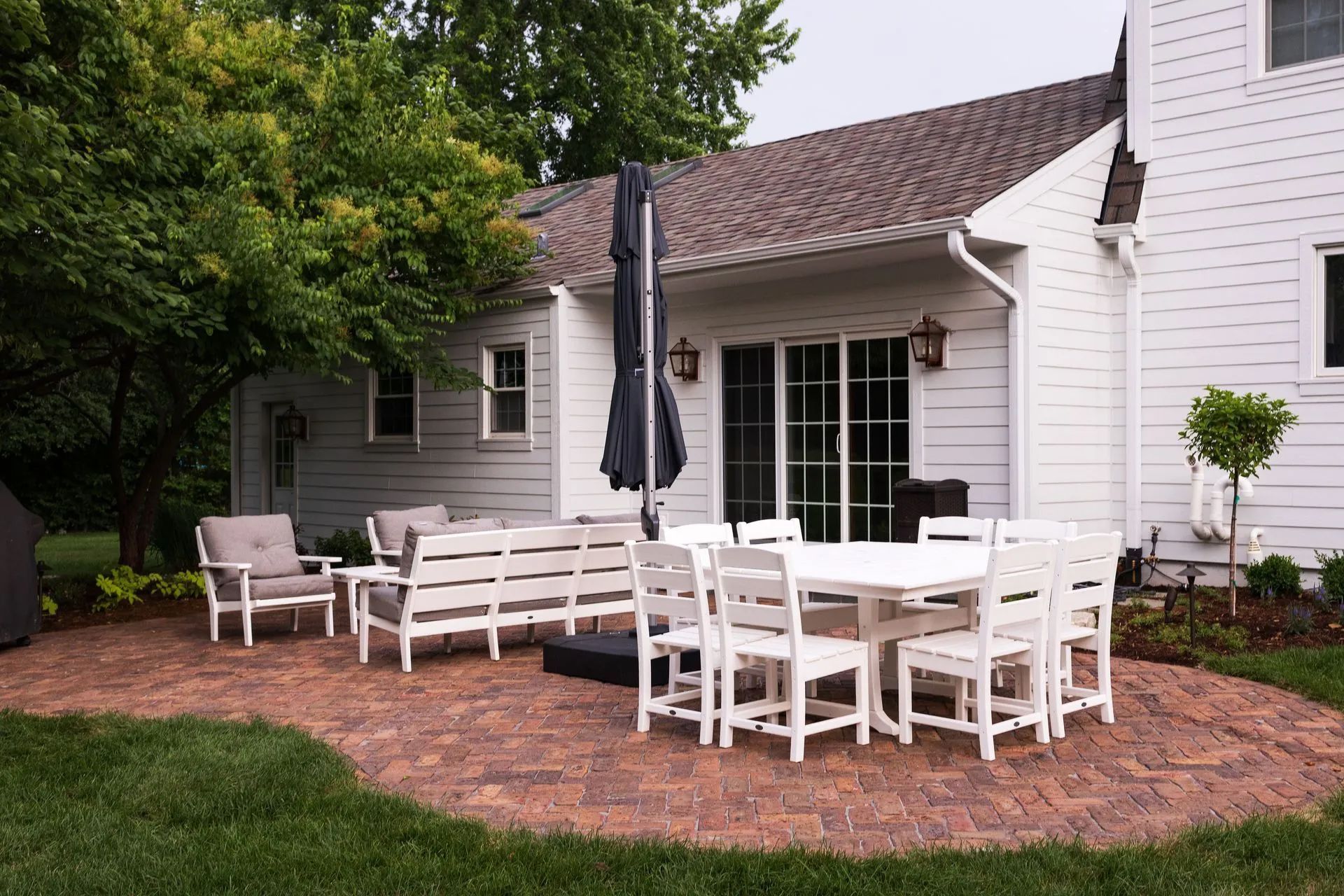 Patio with white outdoor furniture, umbrella, and a brick patio beside a white house.