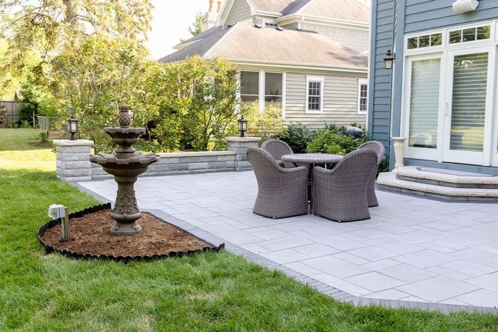 Backyard patio with a fountain, table, and chairs; grass and a blue house in the background.