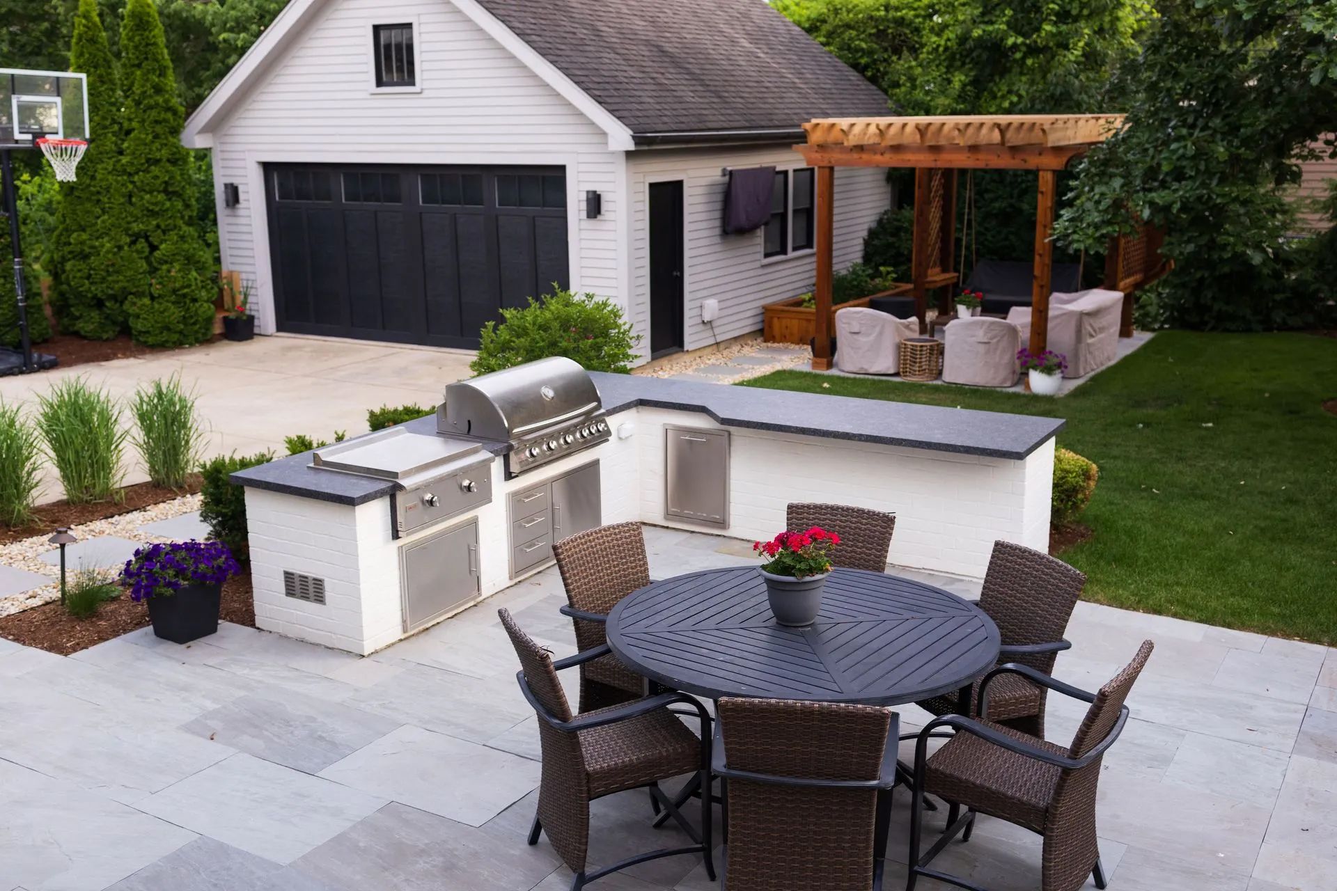 Outdoor kitchen with grill, bar, and round table on patio near a garage.