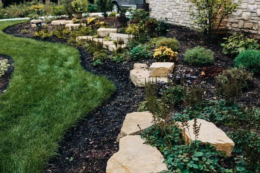 Landscaped yard with steps, plants, dark mulch, and green grass.