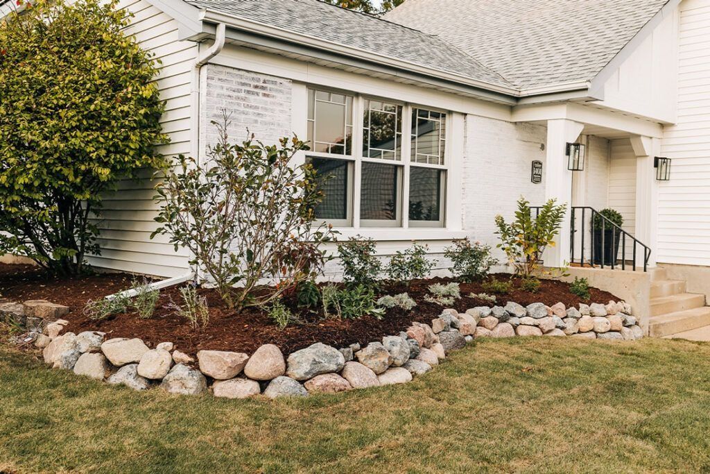 White house with stone retaining wall, mulch, and landscaping in front yard.