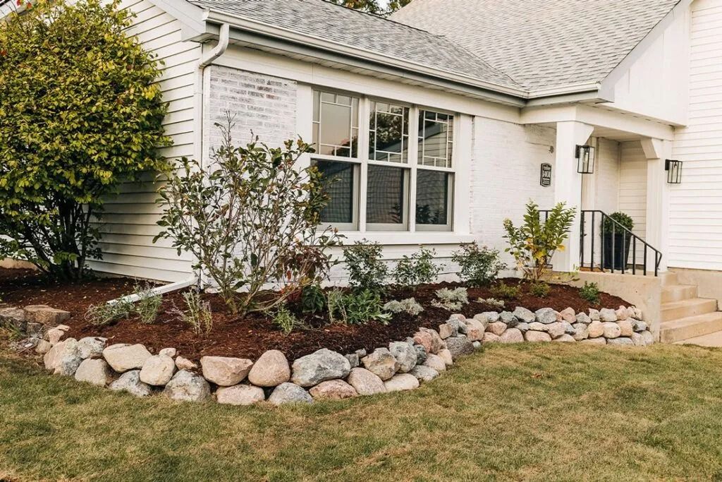 White house with stone-edged flower bed, green lawn, and landscaping.