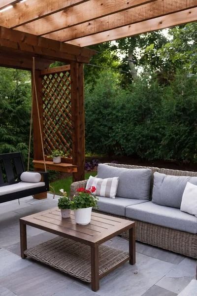 Patio with seating, swing, and wooden pergola, surrounded by lush greenery.