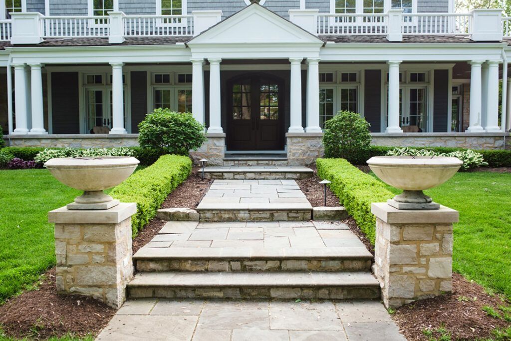 Stone steps leading to a large house with a porch, columns, and landscaping.