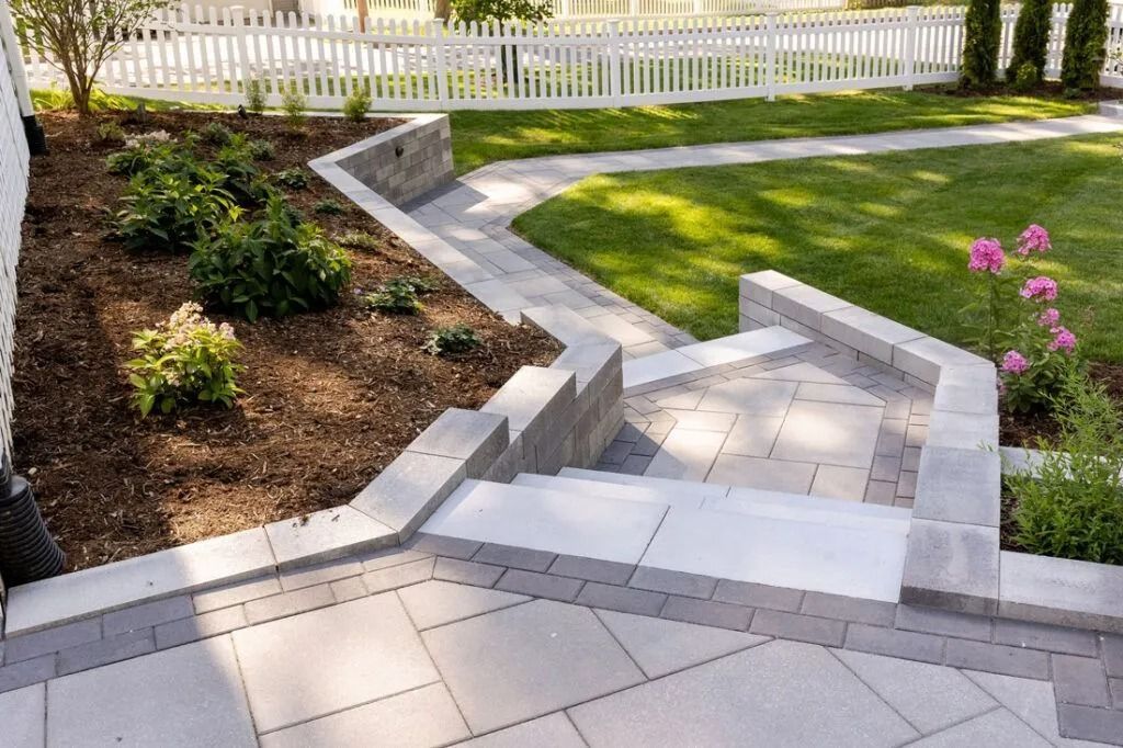 Gray stone steps and walkway in a landscaped yard, leading to a white picket fence.