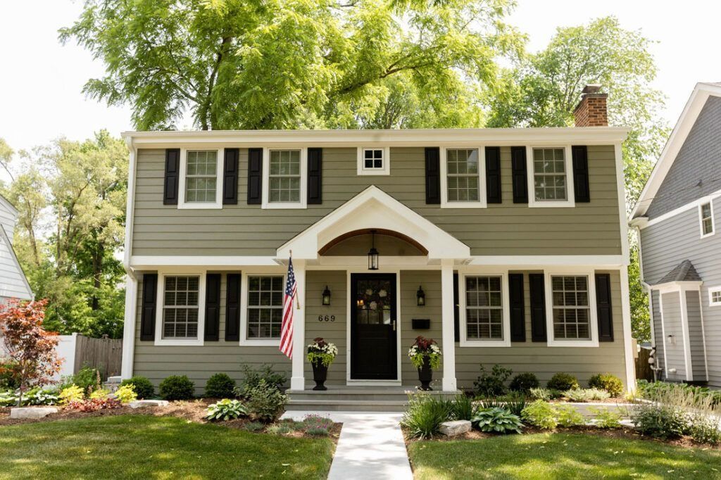 Two-story green house with black shutters, white trim, and a small porch. An American flag hangs by the front door.