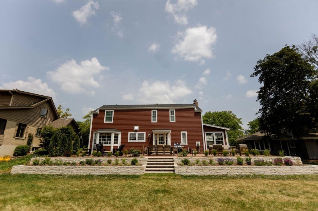 Red brick house with white trim, facing a grassy lawn under a cloudy blue sky.