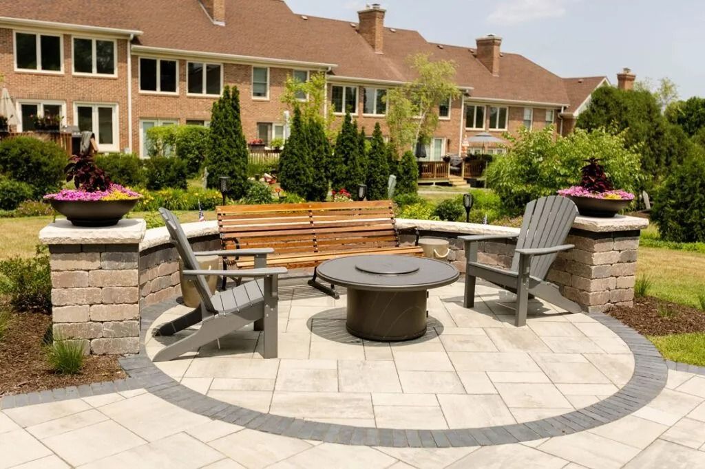 Outdoor patio with gray chairs, fire pit, and planters. Brick buildings are in the background.