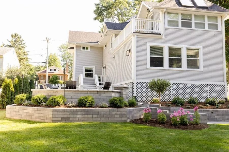 Gray house with backyard patio and retaining walls, lush lawn, and trees.